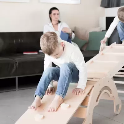 Brinquedo de madeira claro para crianças com barras para agarrar e sofá ao fundo