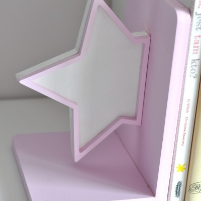 Apoio para livros em forma de estrela rosa e branco ao lado de livros sobre superfície branca