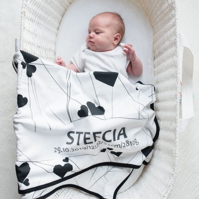 Bebé numa cesta branca com manta branca e preta com texto Stefcia.