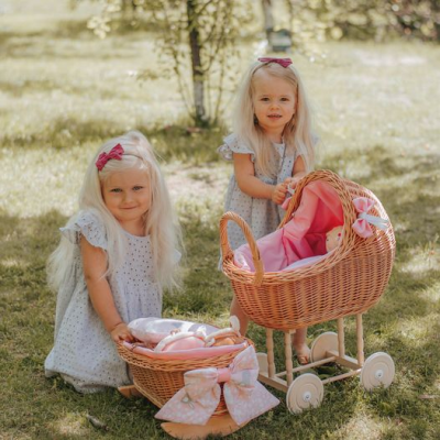 Crianças brincando com carrinhos de bebé de vime cor de rosa em jardim