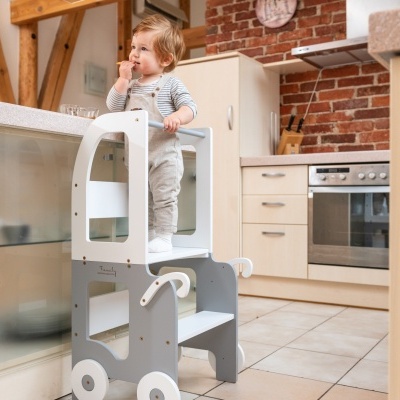 Criança em torre de aprendizagem branca e cinza em cozinha moderna