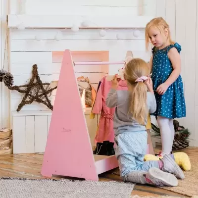 Duas crianças brincam com cabideiro rosa em sala decorada para Natal.