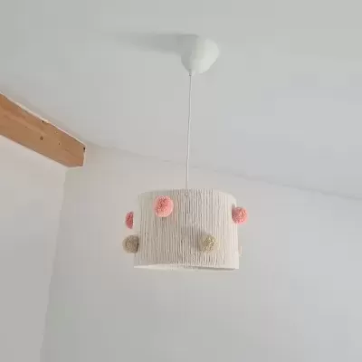 Candeeiro de teto pendente branco com pompons coloridos, em ambiente interior com parede branca e vigas de madeira
