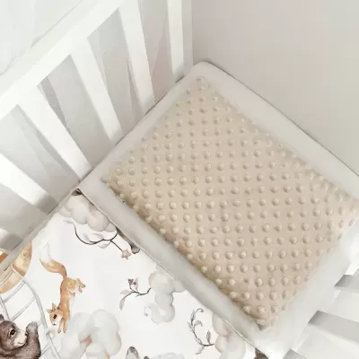 Berço branco com almofada bege e cobertor estampado com animais em cama de bebê.