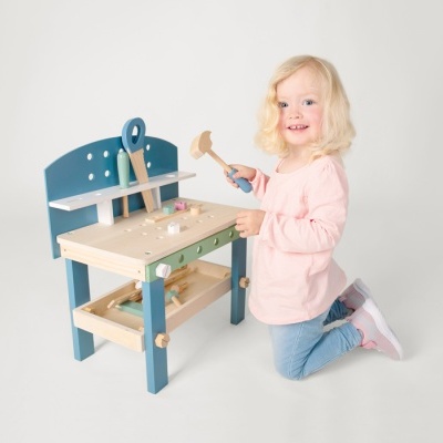Menina brinca com banco de trabalho de madeira azul e natural