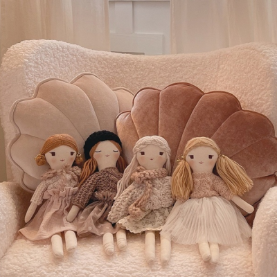 Quatro bonecas de tecido sentadas numa poltrona branca com almofadas em formato de concha.