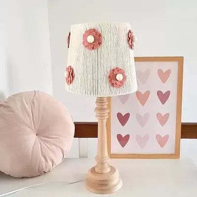 Candeeiro branco com flores rosa e base em madeira clara ao lado de almofada rosa e quadro com corações