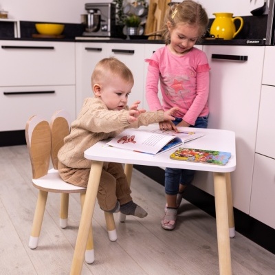 Mesa branca com pernas de madeira clara e cadeira infantil com encosto em forma de asas de anjo
