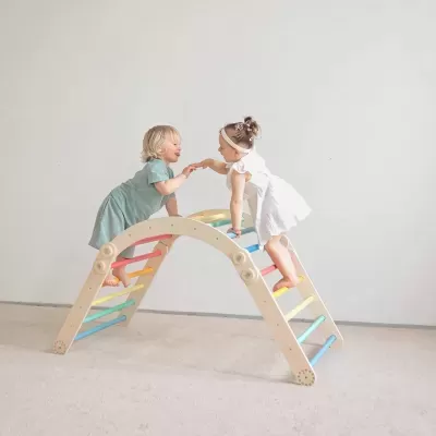Crianças pequenas a brincar em escorrega de madeira com barras coloridas em ambiente interior