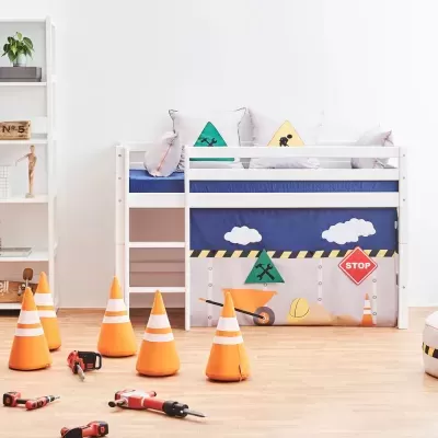 Cama infantil branca com cortina temática de construção e cones de trânsito laranja no chão