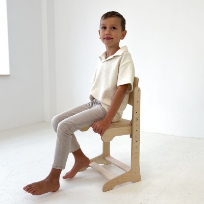 Criança sentada numa cadeira de madeira clara ajustável em ambiente branco