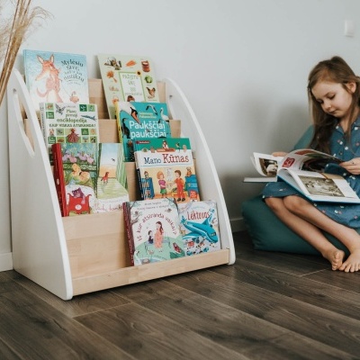 Expositor branco de madeira com livros infantis e criança sentada lendo