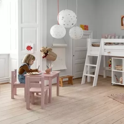 Quarto infantil com mesa e cadeiras rosas, cama alta branca e luminárias de papel penduradas