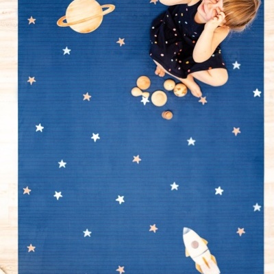 Tapete azul com estrelas, planeta Saturno e foguetão, criança sentada com vestido azul