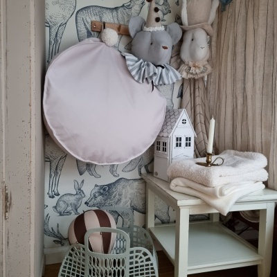 Decoração infantil com cabeças de pelúcia penduradas, almofada rosa, mesinha branca com toalhas e candelabro, bolsas e parede com estampa de animais.