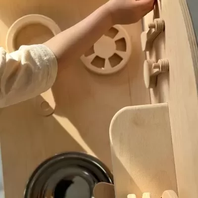 Mini cozinha de brinquedo em madeira clara com botões e pia metálica com mão de criança