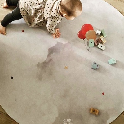 Tapete redondo cinza com padrão de nuvens e estrelas coloridas, bebé a rastejar e brinquedos de madeira