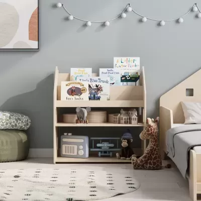 Estante baixa de madeira clara com livros infantis e brinquedos, junto a cama num quarto com parede cinza.