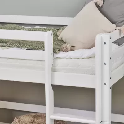Cama de beliche branca com escada, cobertor verde e almofadas com pompons