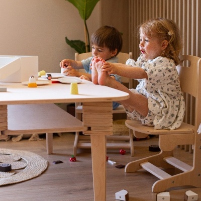 Mesa e cadeiras de madeira para crianças com crianças a brincar.
