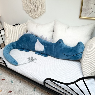 Pelúcia de crocodilo azul num sofá branco com almofadas e decoração na parede