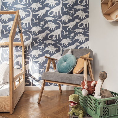 Cadeira com almofadas, papel de parede de dinossauros, cama de madeira e carrinho verde com brinquedos.