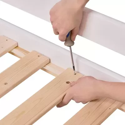 Mãos a montar estrado de cama em madeira clara com parafusos e chave de fendas