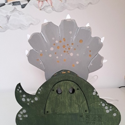 Figura decorativa de dinossauro verde em madeira com detalhes cinza e laranja, sobre superfície branca.