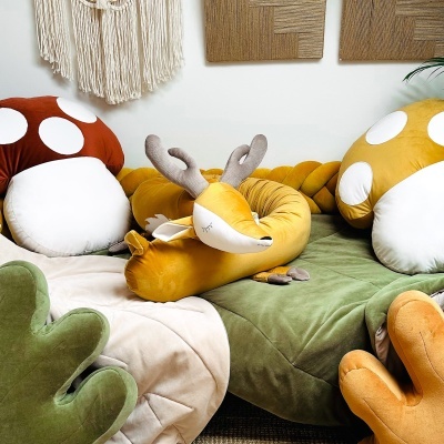 Conjunto de almofadas de raposa e cogumelos em tecido macio em amarelo, branco, verde e castanho numa cama ou sofá.