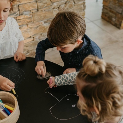 Crianças a desenhar numa mesa preta com giz colorido