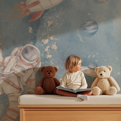 Parede com desenho espacial atrás de cama com almofada branca, ursinhos de peluche e criança sentada a ler.