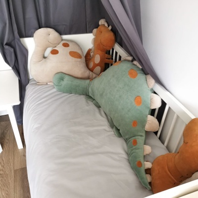 Peluches de dinossauros coloridos num berço branco com cortinas cinzentas