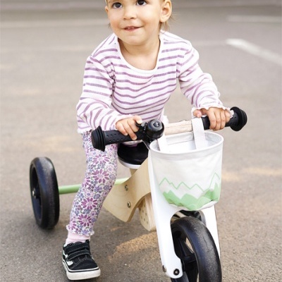 Criança em bicicleta de equilíbrio de madeira com saco branco e padrão verde
