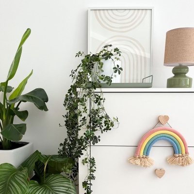 Comoda branca com plantas, candeeiro, quadro e enfeite de parede arco-íris.
