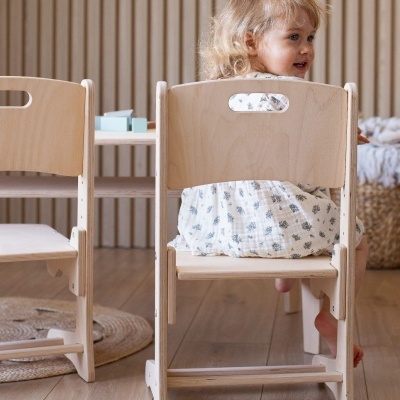 Cadeira infantil de madeira clara com criança sentada de costas e vestido branco com padrão floral
