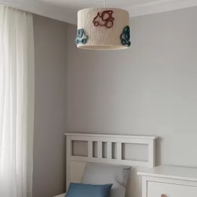 Quarto com cama branca, almofadas cinza e azul, candeeiro de teto bordado com carros, parede cinza e cómoda branca.