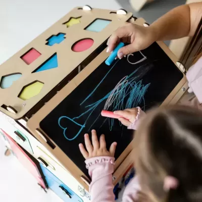 Cuboda de atividade em madeira com figuras coloridas e quadro-negro com desenhos a giz feitos por crianças