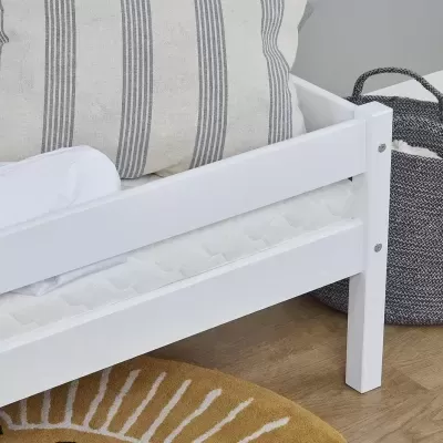 Cama de criança branca com almofadas, manta, peluche e cesto cinza ao lado