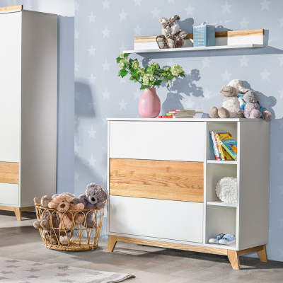 Cómoda branca com detalhes em madeira e peluches num quarto infantil com papel de parede azul com estrelas