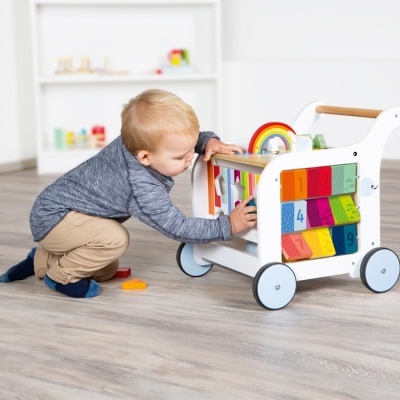 Bébé com carrinho de madeira branco e colorido numa divisão interior clara com chão de madeira