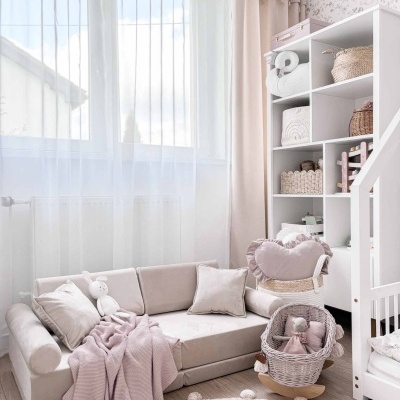 Sofá infantil bege com almofadas e manta rosa numa sala clara com prateleira branca e brinquedos