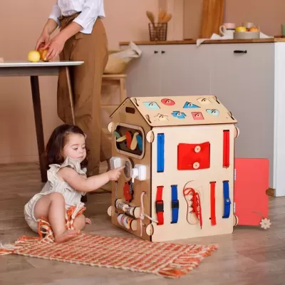 Brinquedo educativo de madeira em forma de casa com elementos interativos coloridos e criança a brincar