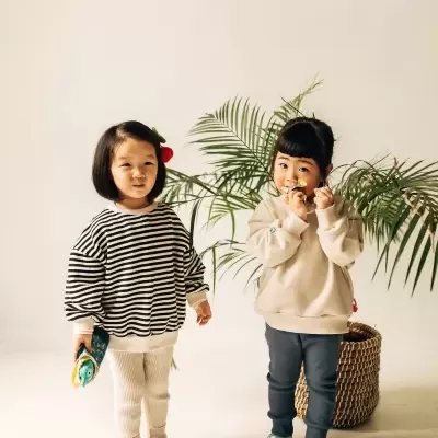 Duas crianças com roupa casual confortável em fundo claro com planta decorativa