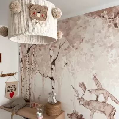Candeeiro de tecto infantil com desenho de urso e pompons, em quarto decorado com pintura de animais e árvores na parede.