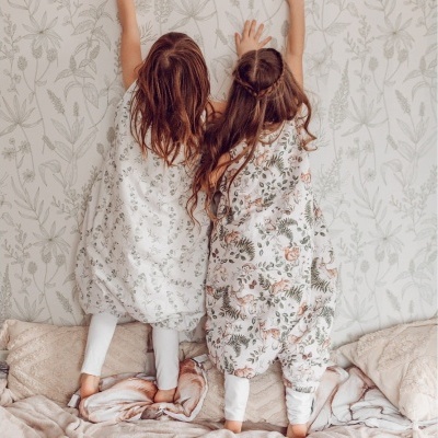 Bebés com sacos de dormir botânicos numa cama com almofadas claras