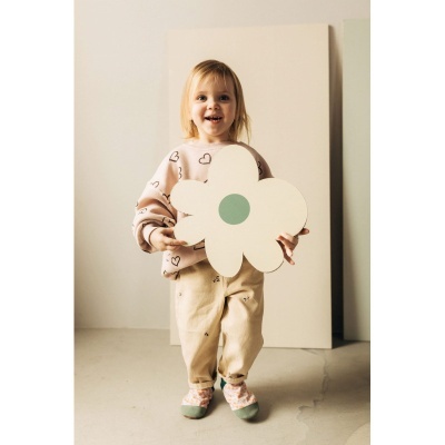 Menina pequena com camisola rosa e calças bege segurando flor decorativa branca