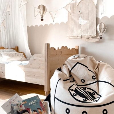 Quarto infantil com cama de madeira clara, pufe estampado, cesta com livros e decoração de balões de ar quente