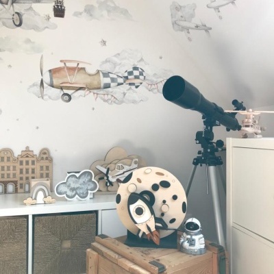 Quarto infantil com decoração de parede de balões e aviões, telescópio preto, brinquedo de foguete e astronauta, caixa de madeira