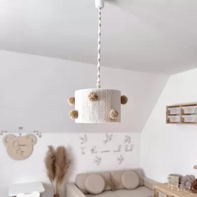 Candeeiro de tecto branco com pompons suspenso numa sala clara com sofá bege e decoração neutra.