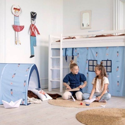 Quarto infantil com cama alta branca, cortina azul de soldadinhos, tenda azul e duas crianças sentadas.